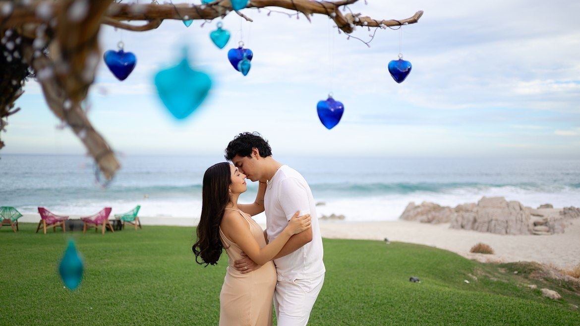A man and woman kissing under a tree with blue hearts from a tree